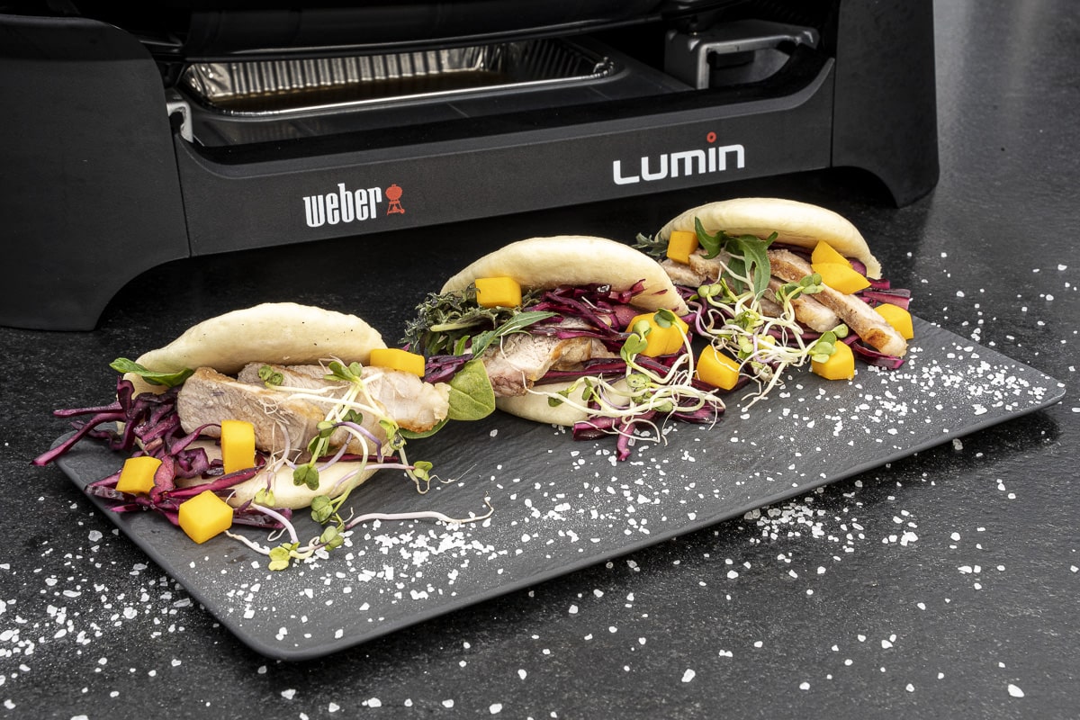 Close-up of a charcoal kettle grill grate showing food placed over the direct heat zone and the indirect heat zone.